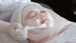 A fat woman receives a procedure of cleaning and lifting the face skin in the beauty salon`s office. The hands of the