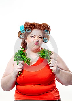 Fat woman with sensuality red lipstick in curlers on a diet holding parsley and dill