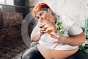 Fat woman sits in chair and eats sandwich, bulimic