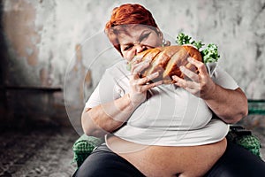 Fat woman sits in chair and eats sandwich, bulimic photo