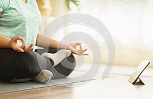 Fat woman sits practicing yoga meditation in sukhasana exercise following a yoga coach through technology tablet at home, Activity