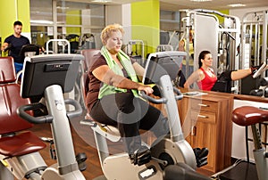 Fat woman training on exercise bike in gym