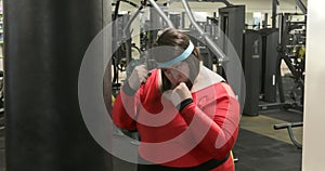 Fat woman trains with a punching bag in the gym.