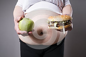 Fat women suffer from obesity with big hamburger and apple in hands, junk food concept