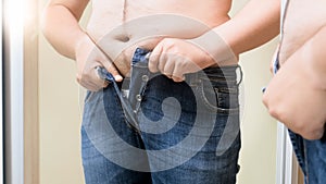 Fat young man trying to fit in small jeans. Concept of male overweight, weight loss and dieting