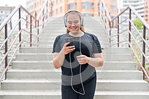 A fat young woman goes down the stairs and listens to music on a smartphone. Obese girl with headphones resting after