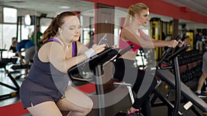 Fat young woman using fitness mobile app while training to lose weight in gym