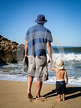 Father and 2 year old son facing ocean waves at the beach from b