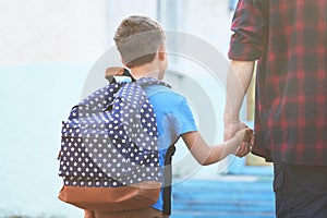Father accompanies the child to school. a man with a child removed from the back. doting dad holding the hand of her son going to