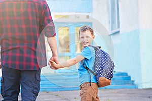 Father accompanies the child to school. a man with a child removed from the back. doting dad holding the hand of her son going to