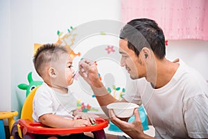 Father acting Mom feeding his son baby 1 year old on chair