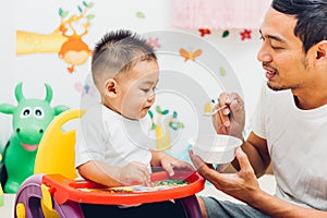 Father acting Mom feeding his son baby 1 year old on chair