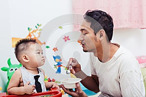 Father acting Mom feeding his son baby 1 year old on chair