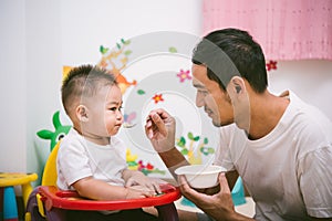 Father acting Mom feeding his son baby 1 year old on chair