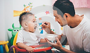 Father acting Mom feeding his son baby 1 year old on chair