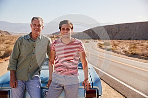 Father and adult son on road trip leaning against their car