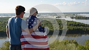 Father with American flag embraces his son on river bank