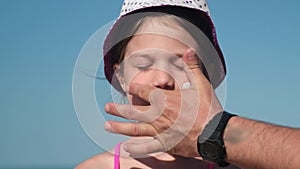 Father apply protective sunscreen on daughter nose at beach on summer vacation