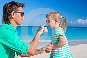 Father apply sunblock cream on his little child nose