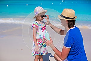 Father apply sunblock cream on his little daughter nose