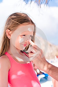 Father applying sun cream to daughter nose.