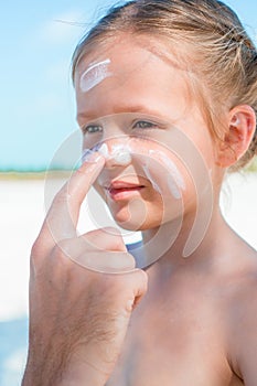 Father applying sun cream to daughter nose.