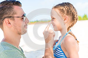 Father applying sun cream to daughter nose. Portrait of cute girl in suncream
