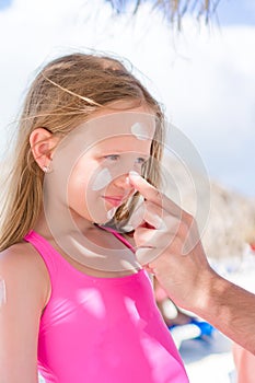 Father applying sun cream to daughter nose. Portrait of cute girl in suncream