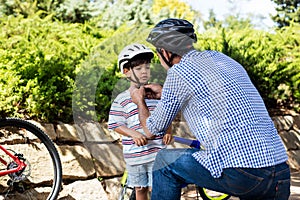 Father assisting son in wearing bicycle helmet in park