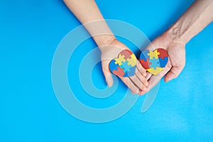 Father and autistic son hands holding jigsaw puzzle heart shape. Autism spectrum disorder family support concept. World