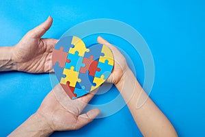 Father and autistic son hands holding jigsaw puzzle heart shape. Autism spectrum disorder family support concept. World