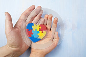 Father and autistic son hands holding jigsaw puzzle heart shape. Autism spectrum disorder family support concept. World