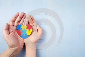 Father and autistic son hands holding jigsaw puzzle heart shape. Autism spectrum disorder family support concept. World