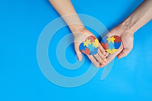 Father and autistic son hands holding jigsaw puzzle heart shape. Autism spectrum disorder family support concept. World