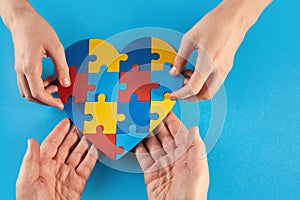 Father and autistic son hands holding jigsaw puzzle heart shape. World Autism Awareness Day