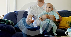 Father and baby boy watching television in living room 4k