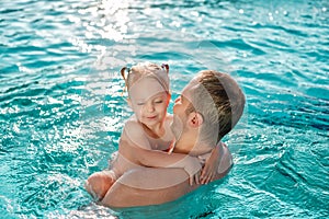 Father with baby daughter having fun on summer vacation splashing In outdoor swimming pool