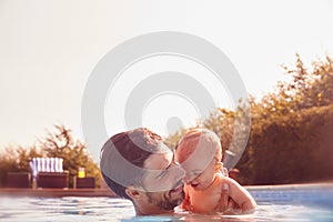 Father With Baby Daughter Having Fun On Summer Vacation Splashing In Outdoor Swimming Pool