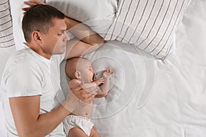 Father and baby sleeping on bed together, top view. Space for text