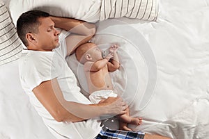 Father and baby sleeping on bed together, top view. Space for text