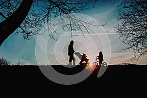 Father with baby in stroller and daughter on runbike walk in sunset nature