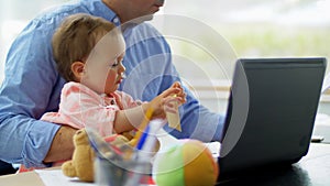 Father with baby working on laptop at home office