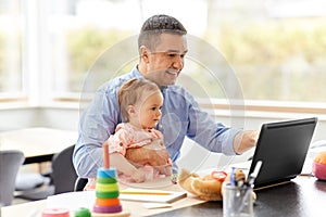 Father with baby working on laptop at home office