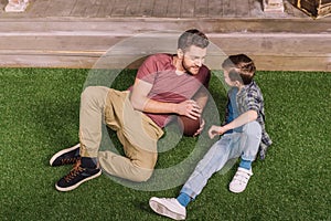 Father with ball and little son laying on the grass at backyard