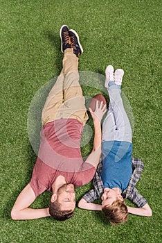 Father with ball and little son laying on the grass at backyard