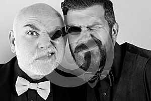 Father and bearded son are fooling around. Glasses for two. Men in suits and bow ties. Soul mates. Family business