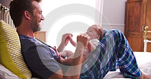 Father In Bed Playing With Newborn Baby Daughter