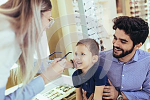 Father with son choosing glasses in optics store. photo