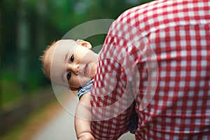 A father carries his little daughter in his arms. The child peeks out from behind Dad`s broad shoulders