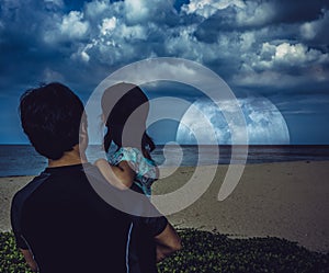 Father carrying daughter and looking at super moon over ocean.